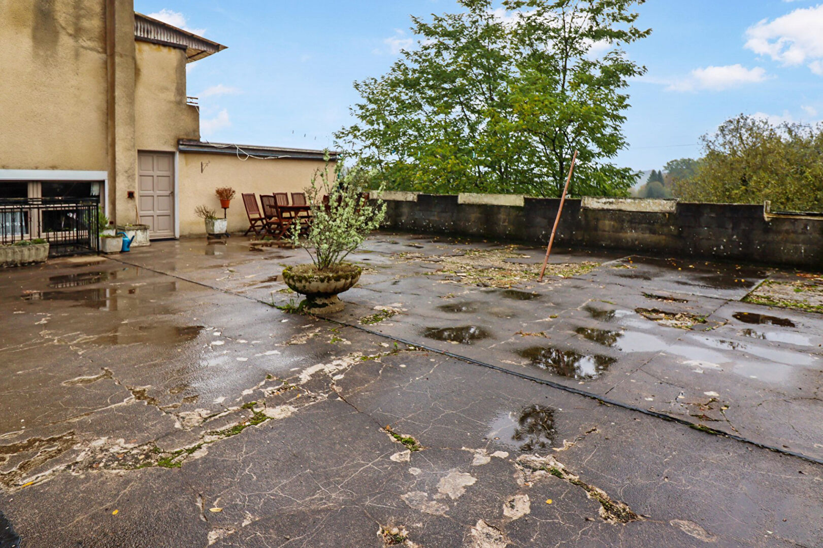 Spacious terrace of a property in Corrèze, Nouvelle-Aquitaine, featuring outdoor seating and overgrown surfaces.