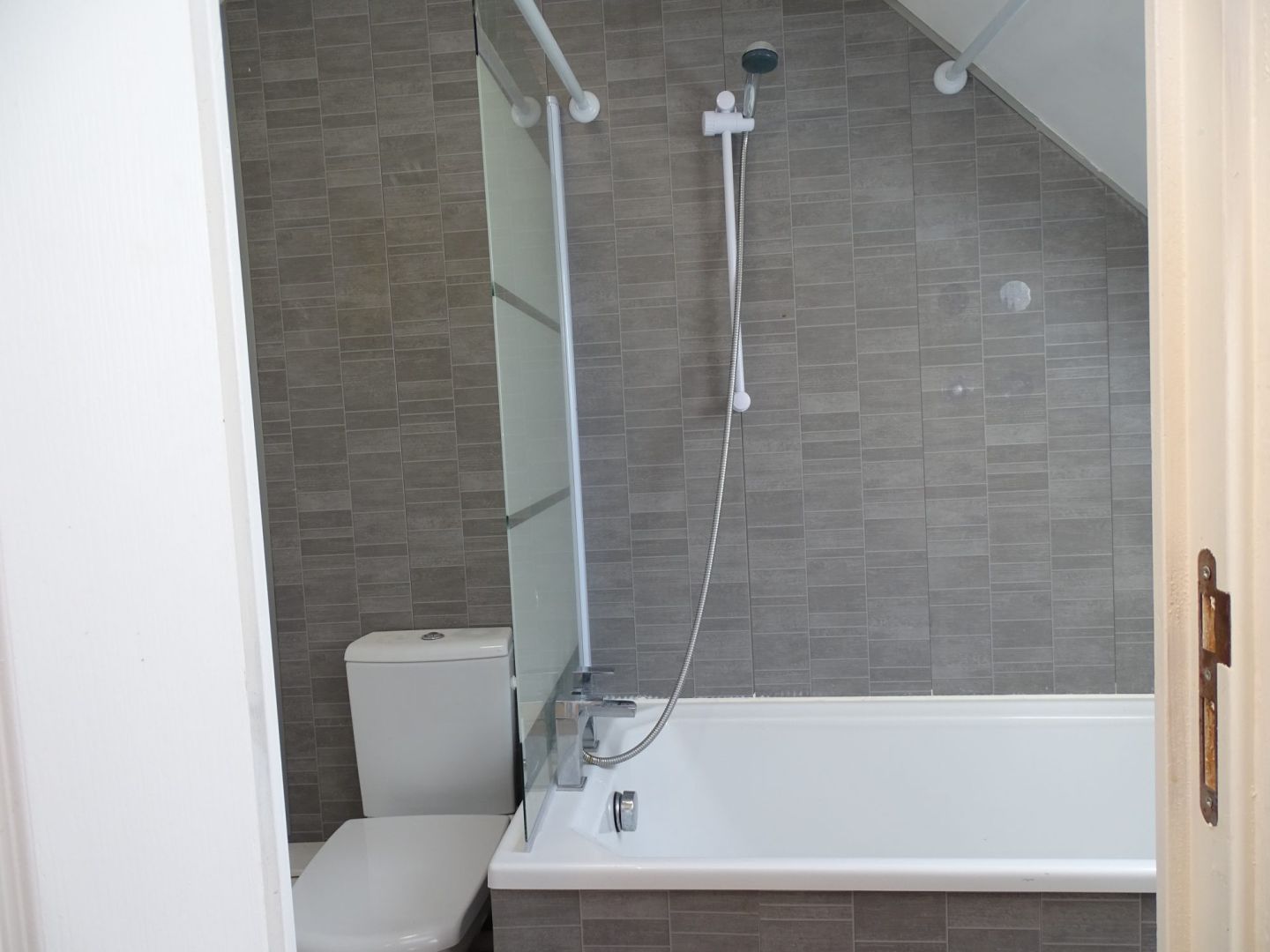 Bathroom with a shower over the bath, modern tiles, and a toilet in Côtes-d'Armor, Brittany, 22110.