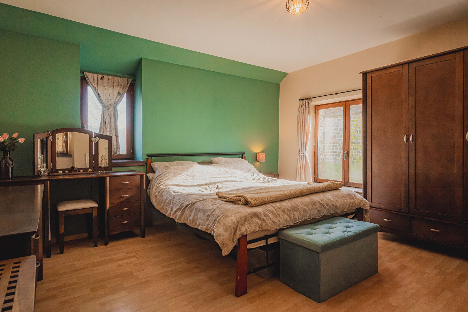 Bright bedroom with wooden furniture and green walls in Orne, Normandy, featuring a double bed and large window.