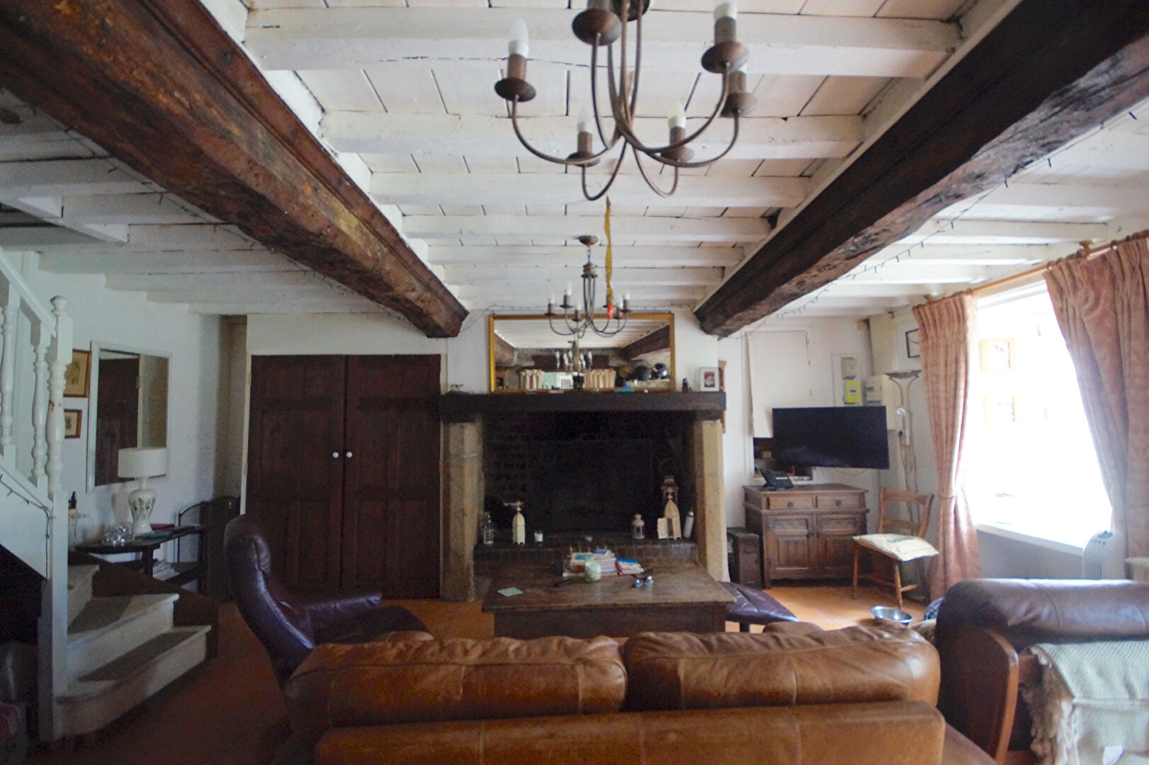 Spacious interior of a property in Manche, Normandy, featuring wooden beams and a cosy fireplace area.