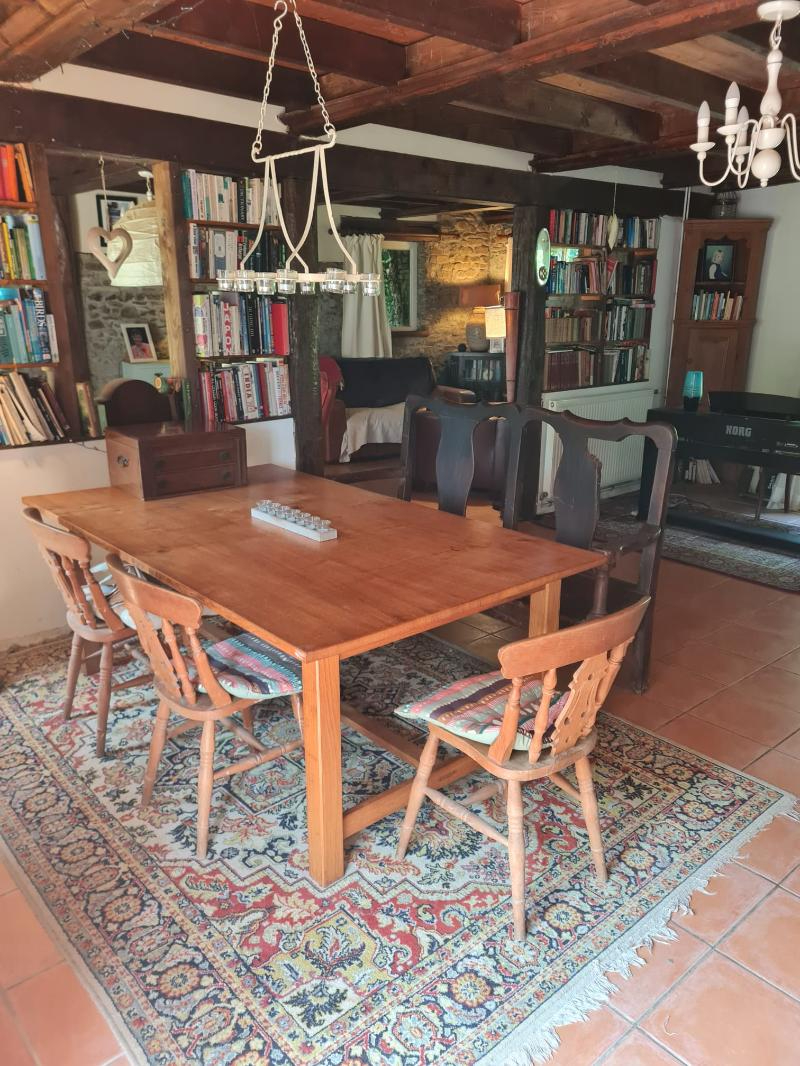 Dining area with wooden table and chairs, bookshelves, and stone walls in a property located in Manche, Normandy.