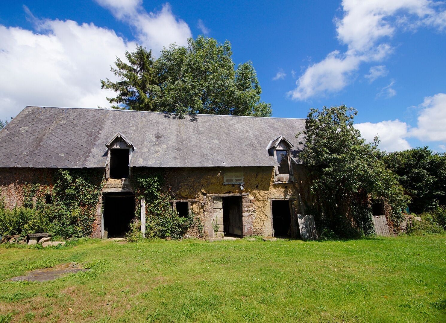 Four-bedroom property in Manche, Normandy, featuring a rustic stone exterior and overgrown garden space.