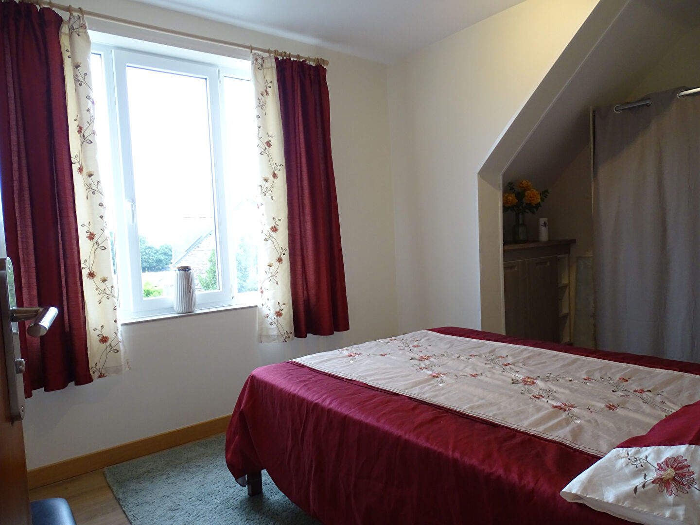 Bright bedroom with floral curtains and a double bed in Finistère, Brittany, featuring three bedrooms in total.