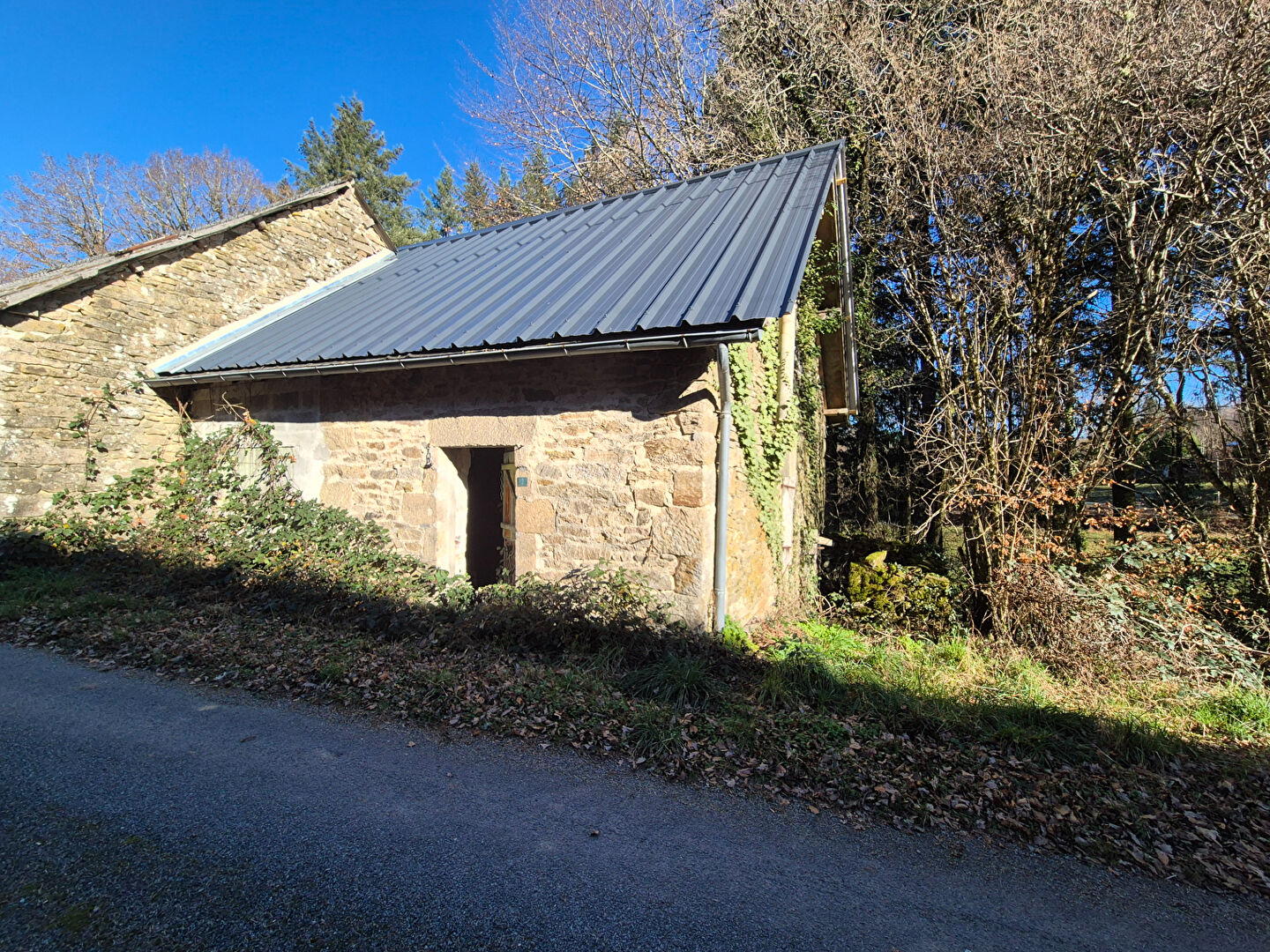 Stone property with a sloped roof situated in Corrèze, Nouvelle-Aquitaine, surrounded by greenery.