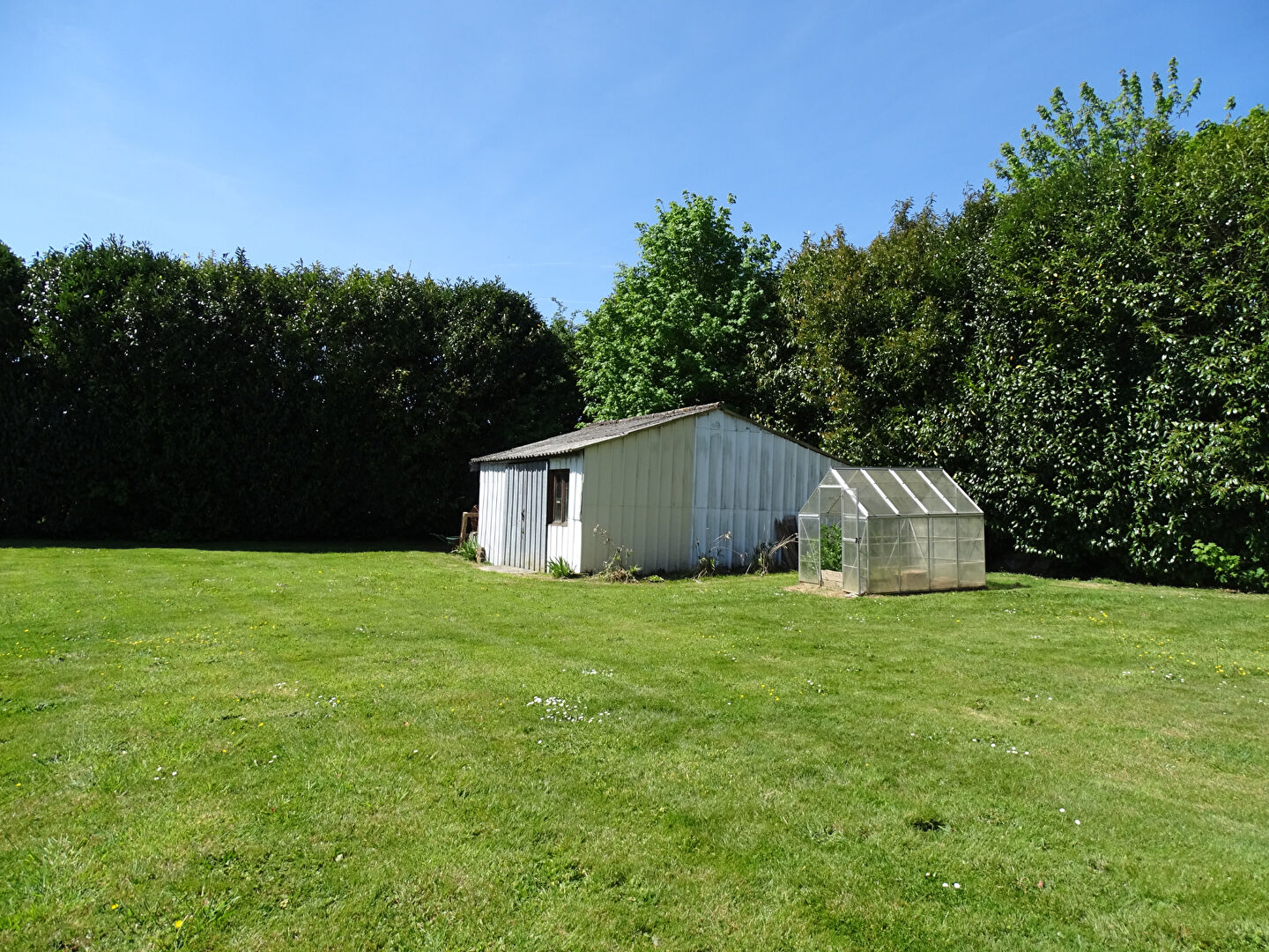 Property in Finistère, Brittany with a garden, shed, and greenhouse surrounded by greenery.