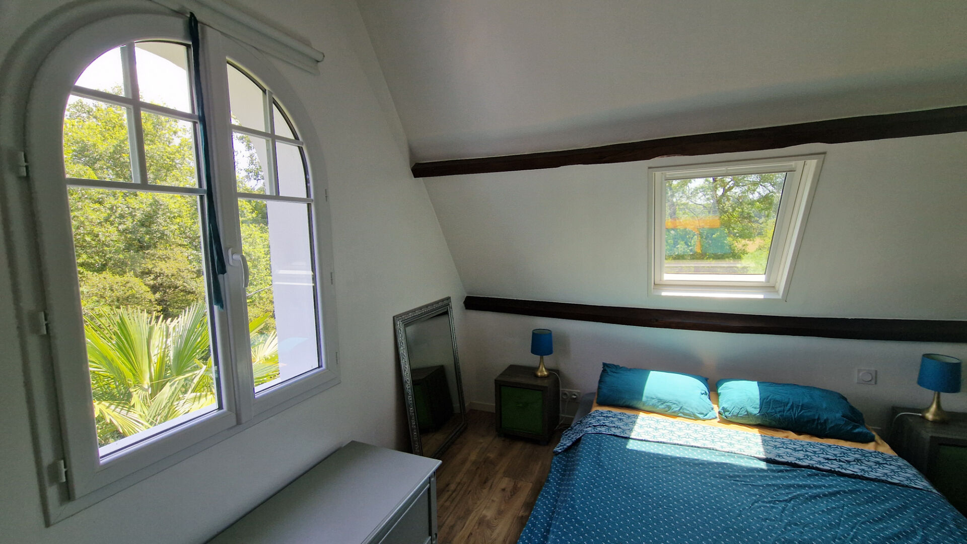 Bright bedroom with large windows, featuring a double bed and wooden beams, located in Côtes-d'Armor, Brittany.
