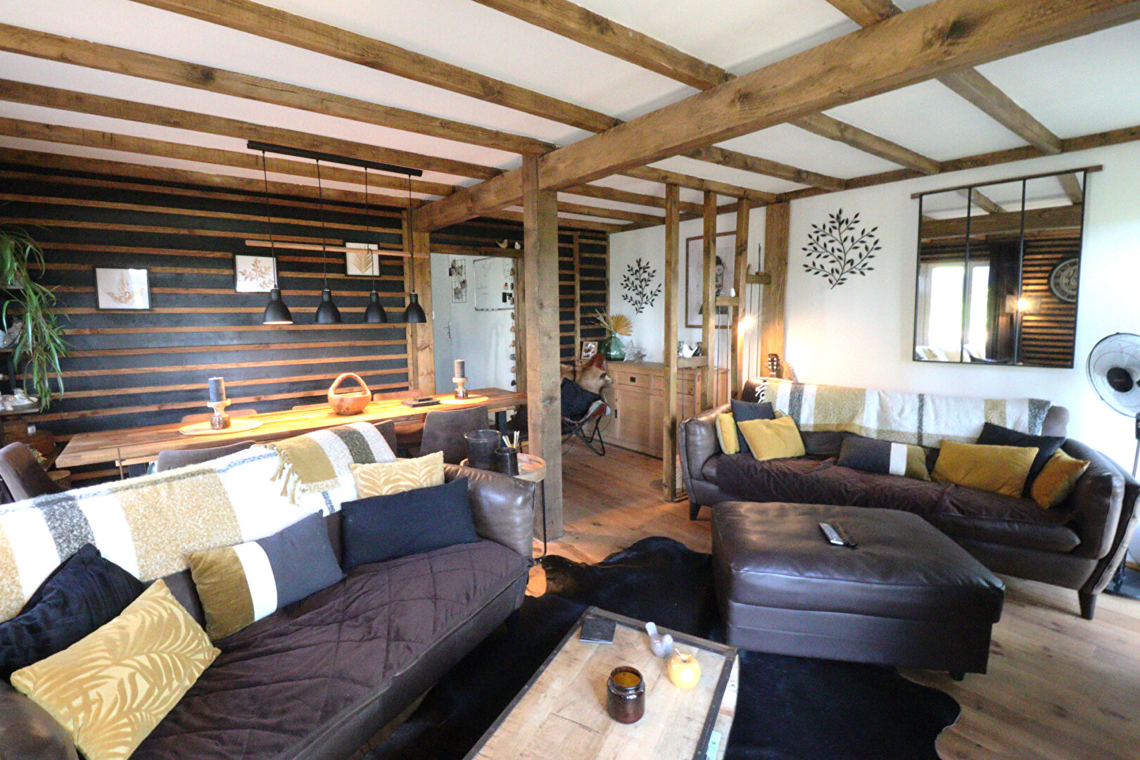 Spacious lounge with wooden beams, cosy sofas, and dining area in a property located in Corrèze, Nouvelle-Aquitaine.