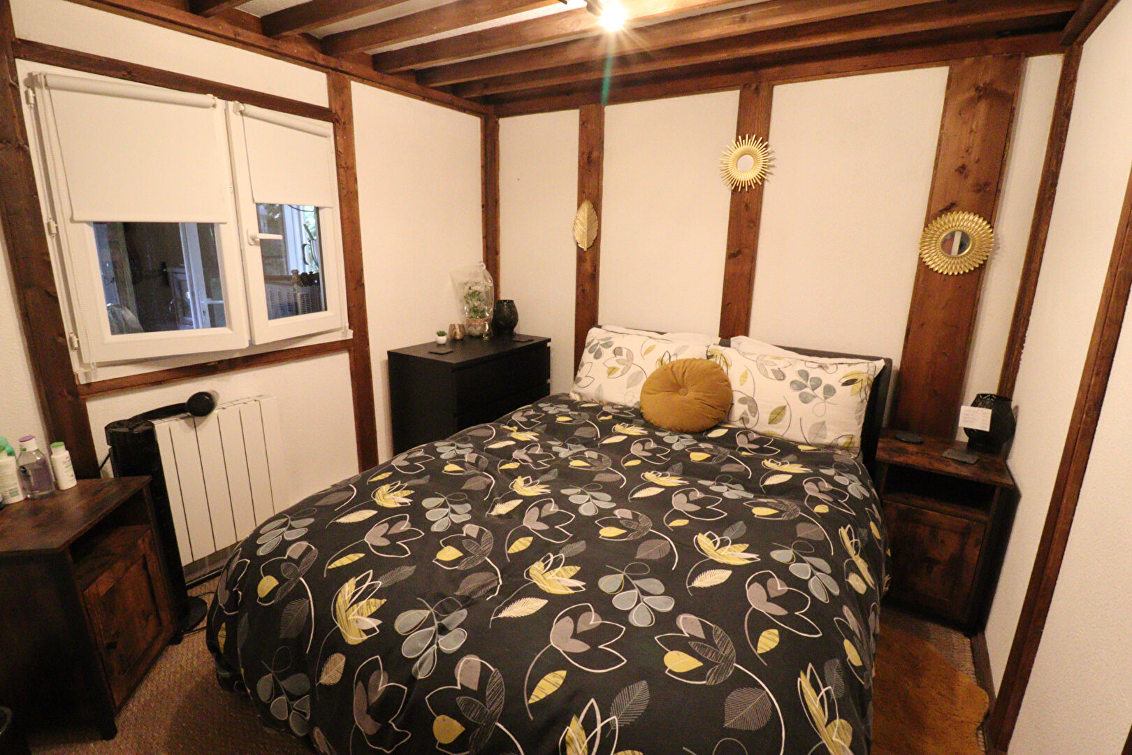 Cosy bedroom in a property located in Corrèze, Nouvelle-Aquitaine, featuring wooden beams and floral bedding.