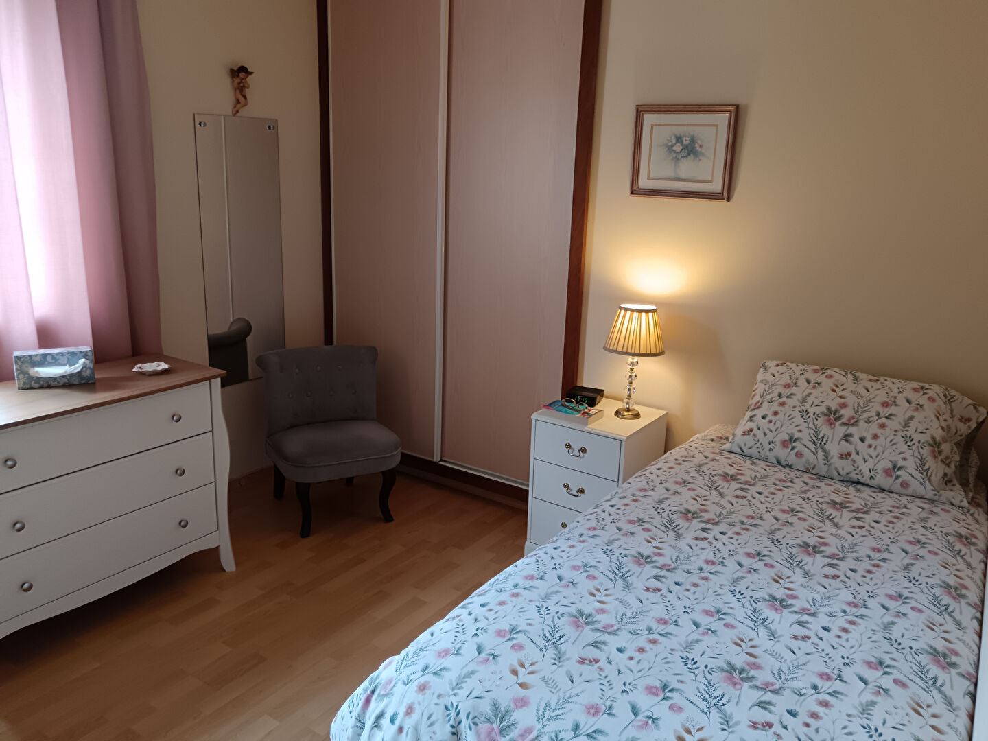 Bright bedroom featuring floral bedding, bedside lamp, and storage in a property located in Manche, Normandy.