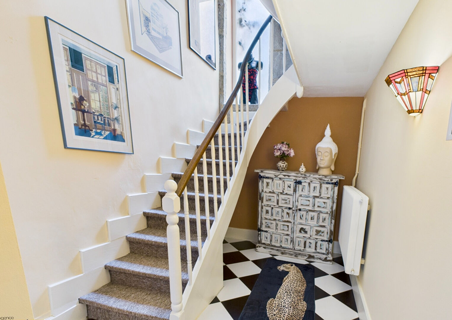Spiral staircase leading to upper levels of the property in Lot, Occitanie, featuring light-filled walls and art displays.
