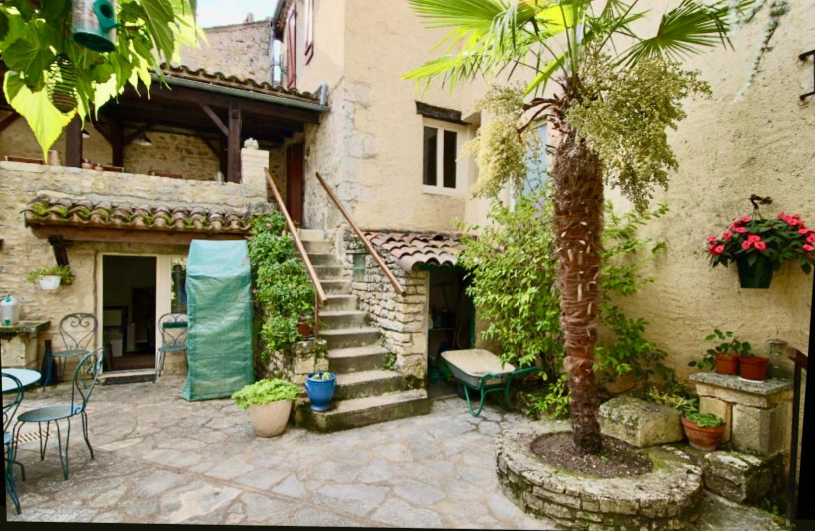 Charming property in Lot, Occitanie, featuring a courtyard with stone steps, palm tree, and outdoor seating area.