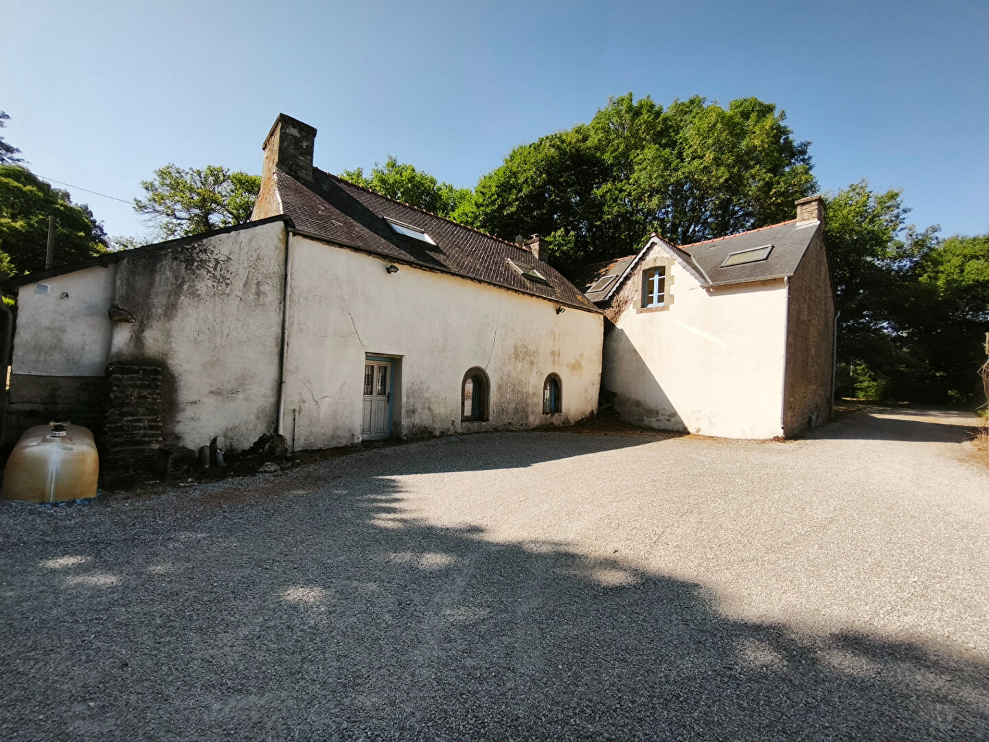 Three-bedroom property in Morbihan, Brittany, featuring a gravel driveway and rustic architecture surrounded by trees.